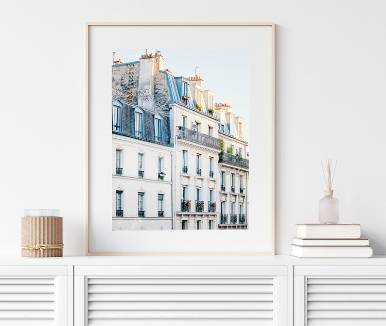 Puede incluir: Una fotograf&iacute;a enmarcada de un edificio blanco con m&uacute;ltiples ventanas y balcones en Par&iacute;s, Francia. El edificio tiene un techo azul claro y est&aacute; rodeado de otros edificios.