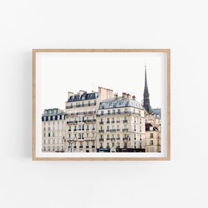 May include: A photograph of a Parisian cityscape with a view of several white buildings with black roofs and windows. The buildings are lined up next to each other and a tall, dark spire is visible in the background.