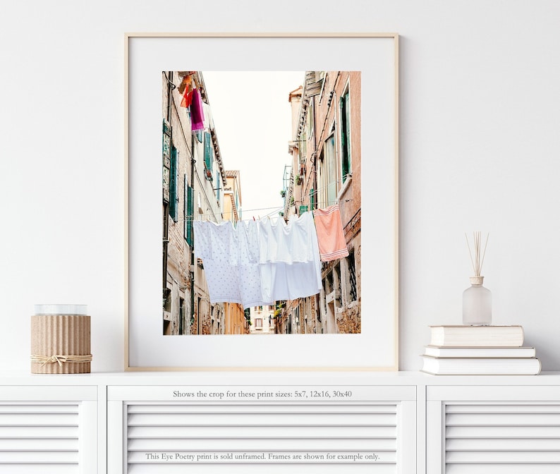 Pu&ograve; includere: Una fotografia di un vicolo stretto a Venezia, Italia. Lenzuola bianche sono appese a uno stendino teso tra gli edifici. Gli edifici sono dipinti in tonalit&agrave; di rosa e giallo.