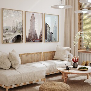 K&ouml;nnte beinhalten: Ein hellbeiges Ecksofa mit drei Kissen, einem Holzrahmen und einer gewebten Textur. Das Sofa steht in einem Wohnzimmer mit drei gerahmten Schwarzwei&szlig;-Stadtansichten, einem Holz-Couchtisch und einem geflochtenen Hocker.