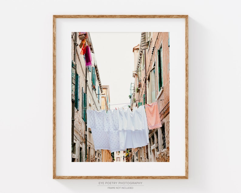 Pu&ograve; includere: Una fotografia di una stretta via a Venezia, Italia, con biancheria bianca appesa a uno stendino tra gli edifici. Gli edifici sono dipinti in tonalit&agrave; di rosa e giallo, e la biancheria sventola nella brezza.