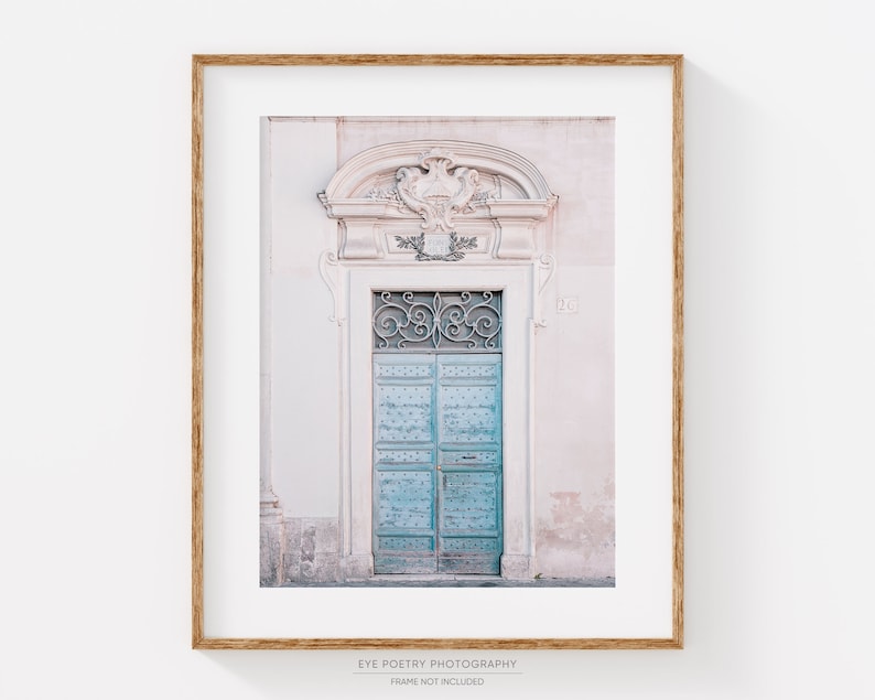 May include: A vintage-style, light blue door with ornate ironwork and a decorative archway above. The door is set against a pale pink wall with a number "120" visible.
