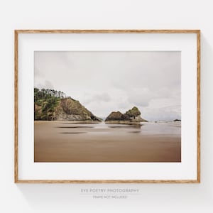 May include: A framed photograph of a beach scene with two rocky outcroppings and a cloudy sky. The sand is wet and the water is calm.