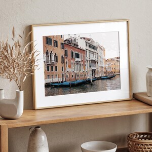 May include: A framed photograph of a canal in Venice, Italy. The photo shows a row of colorful buildings along the canal, with gondolas docked in the water.