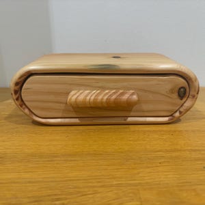 May include: A wooden box with a drawer and a carved wooden handle. The box is made of light wood with a natural finish.