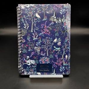May include: A spiral-bound notebook featuring a dark blue background with a repeating pattern of Harry Potter-themed illustrations including owls, a castle, and a dog. A rectangular label at the bottom displays the text Harry Potter and Vera Bradley.