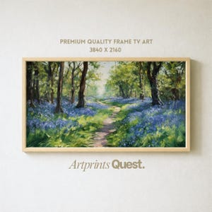 Op de afbeelding: Een ingelijst landschapsschilderij toont een pad door een bos met blauwe bloemen. Het kunstwerk zit in een lichte houten lijst. De tekst "PREMIUM QUALITY FRAME TV ART 3840 X 2160" staat bovenaan en "Artprints Quest" onderaan.