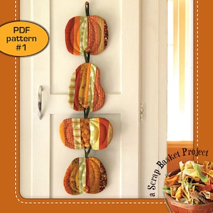 May include: A PDF pattern for making pumpkin-shaped coasters. The pattern is called "Pumpkin Coasters" and is part of a "Scrap Basket Project". The image shows four finished coasters hanging on a white door.