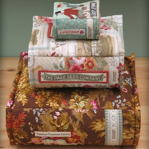 May include: A stack of fabric boxes with floral patterns. The top box is labelled "Easy Sewing" and the second box is labelled "Couture 2". The bottom box is labelled "The Page Seed Company". The boxes are sitting on a brown fabric cushion with a floral pattern and the label "Timeless Treasures Fabrics".