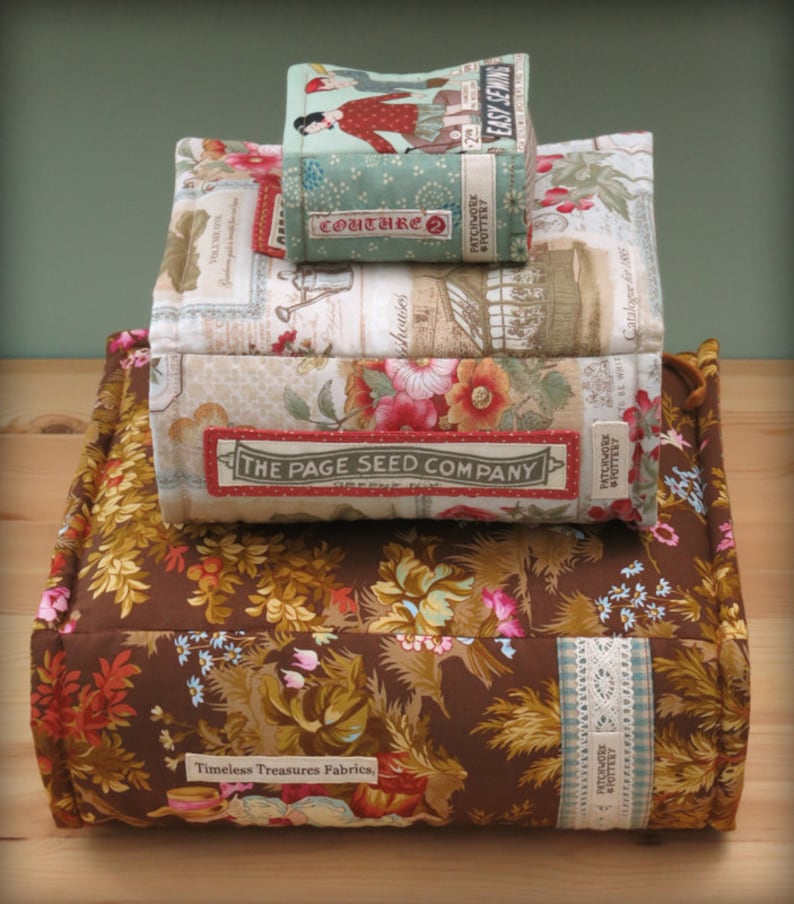 May include: A stack of fabric boxes with floral patterns. The top box is labelled "Easy Sewing" and the second box is labelled "Couture 2". The bottom box is labelled "The Page Seed Company". The boxes are sitting on a brown fabric cushion with a floral pattern and the label "Timeless Treasures Fabrics".
