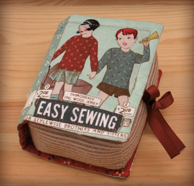May include: A vintage-style book cover featuring a red and blue illustration of two children. The book is titled "Easy Sewing for Stylewise Brothers and Sisters". The cover is made of fabric and has a red ribbon tied around it.