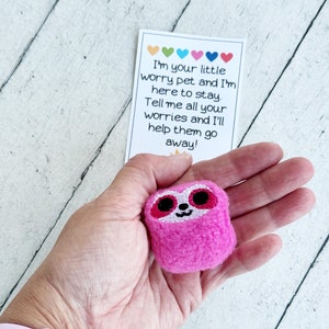May include: Pink plush worry pet with embroidered eyes and a smiling mouth. The pet is holding a card that reads "I'm your little worry pet and I'm here to stay. Tell me all your worries and I'll help them go away!"