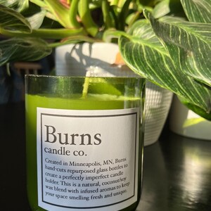 Pu&ograve; includere: Un barattolo di vetro verde per candele con un'etichetta bianca su cui &egrave; scritto "Burns candle co.". L'etichetta include anche il testo "Creato a Minneapolis, MN, Burns taglia a mano bottiglie di vetro riutilizzate per creare un portacandele imperfetto. Questa &egrave; una miscela di cera naturale, cocco e soia, con aromi infusi per mantenere il tuo spazio profumato di fresco e unico."
