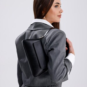Puede incluir: Una mujer con un blazer gris y pantalones con un bolso de hombro de cuero negro.