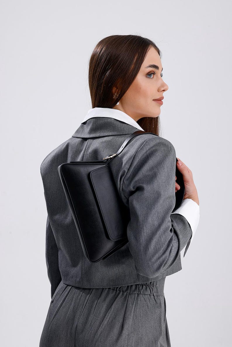 Puede incluir: Una mujer con un blazer gris y pantalones con un bolso de hombro de cuero negro.
