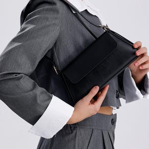 Puede incluir: Un bolso de hombro de cuero negro con cierre de solapa. El bolso tiene una hebilla dorada y una correa larga.