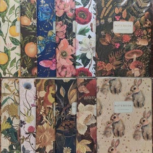 May include: A collection of notebooks with various floral and animal designs. The covers feature illustrations of butterflies, flowers, mushrooms, and rabbits. The notebooks have a variety of colors, including orange, blue, pink, and brown.