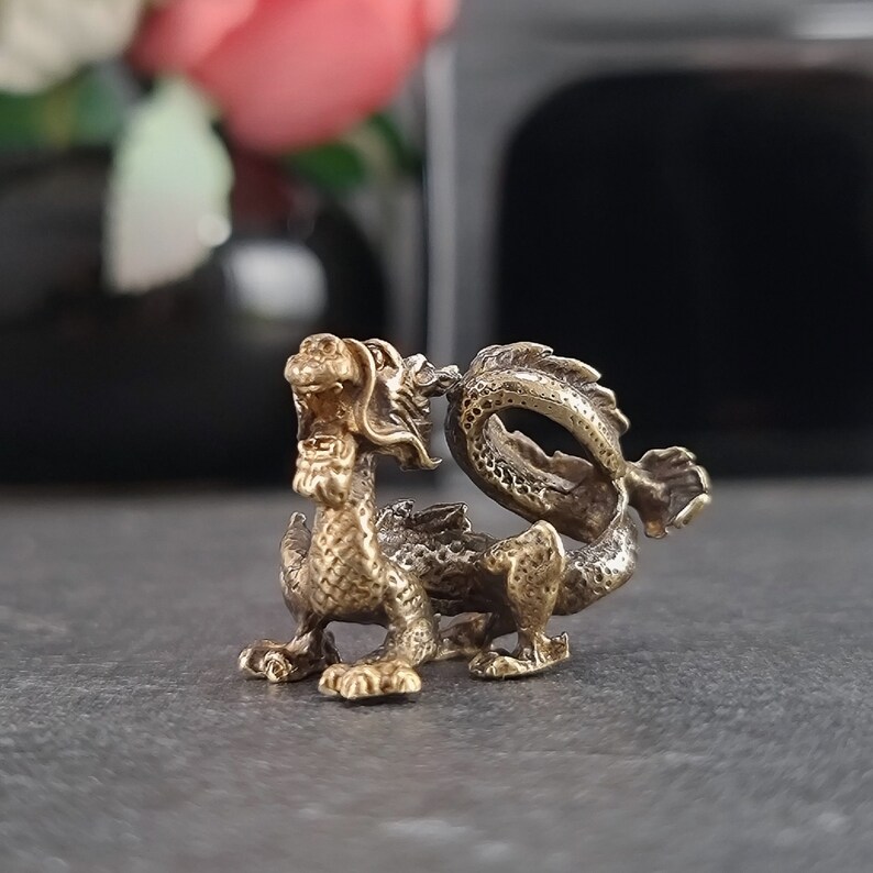 May include: A small, gold-colored brass dragon figurine with a detailed, textured surface. The dragon is curled up with its tail in its mouth.