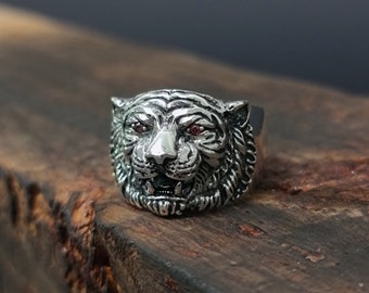 May include: A silver ring featuring a detailed tiger head design. The tiger's eyes are set with red gemstones.