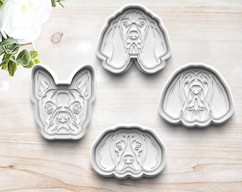 Puede incluir: Cuatro cortadores de galletas de plástico blanco con forma de cabeza de perro. Los cortadores están sobre una superficie de madera clara.