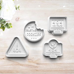 May include: Four white cookie cutters with tech-themed designs. One is a triangle with "404" and an exclamation point. Another is a circle with a bite taken out and the text "I'M DELETING COOKIES". The other two are computer monitor shapes with "404" and "Not Found" text.