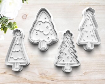 Könnte beinhalten: Vier weiße Plastik-Ausstecher in Form von Weihnachtsbäumen. Die Ausstecher sind in verschiedenen Größen und Formen, mit unterschiedlichen Designs von Ornamenten und Sternen.
