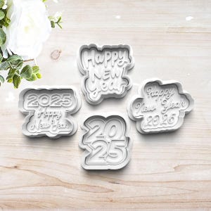 May include: Four white plastic cookie cutters for making New Year's Eve cookies. The cutters are shaped like the numbers 2025 and the words "Happy New Year".