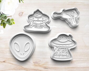 May include: Set of four white plastic cookie cutters shaped like a UFO, an alien head, and a ray gun.
