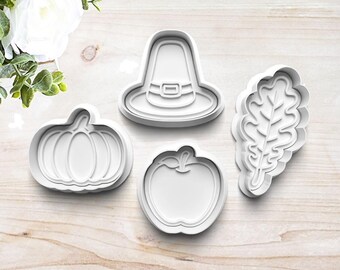 May include: Set of four white plastic cookie cutters shaped like a pilgrim hat, pumpkin, apple, and oak leaf.