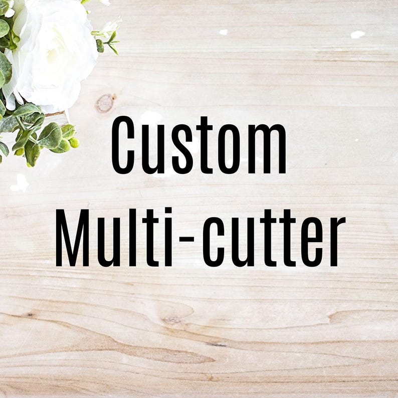 May include: The words "Custom Multi-cutter" are displayed in bold black font against a light wood grain background. White flowers and green foliage are in the upper left corner.