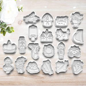May include: A set of 16 white plastic cookie cutters featuring various fairytale and castle themes. The cutters include a crown, a nutcracker, a dragon, a castle, a fairy, a harp, a carriage, a mushroom, a knight, a unicorn, a mirror, a dog, a princess, a prince, a frog, and a house.