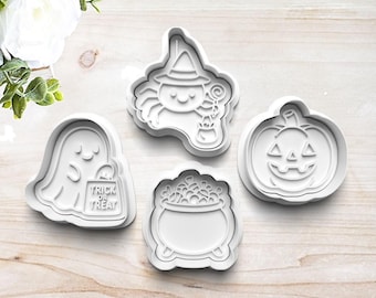 May include: A collection of four white Halloween-themed cookie cutters. The shapes include a ghost holding a bag with "Trick or Treat" text, a witch spider, a jack-o'-lantern, and a cauldron filled with treats. Perfect for baking festive treats.