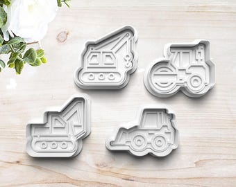 Puede incluir: Conjunto de cuatro cortadores de galletas de plástico blanco con forma de vehículos de construcción: una grúa, una excavadora, una retroexcavadora y un rodillo compactador.