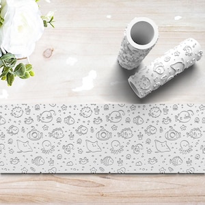 May include: Two white cylindrical paint rollers featuring a raised, embossed pattern of various sea creatures including fish, octopuses, crabs, stingrays, and submarines, shown alongside a flat strip displaying the repeating underwater design.