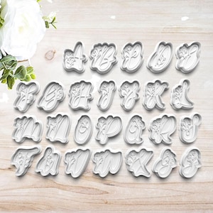 May include: A set of 26 white plastic cookie cutters shaped like the letters of the alphabet with floral accents.