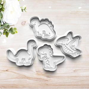 May include: Four white plastic dinosaur cookie cutters. The cutters are shaped like a stegosaurus, a brachiosaurus, a triceratops, and a pterodactyl.
