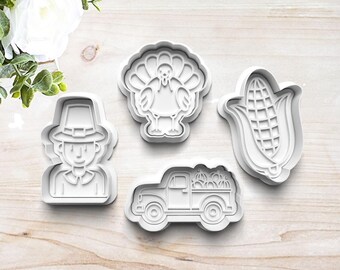 May include: Set of four white plastic cookie cutters shaped like a pilgrim, a turkey, a corn cob, and a pickup truck carrying pumpkins.