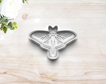 May include: A white plastic cookie cutter shaped like a moth with intricate wing details.