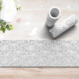 May include: White rolling pins with a pumpkin and leaf pattern, alongside a matching embossed sheet. The design features various pumpkin shapes and fall foliage. Perfect for creating textured patterns on clay or dough.