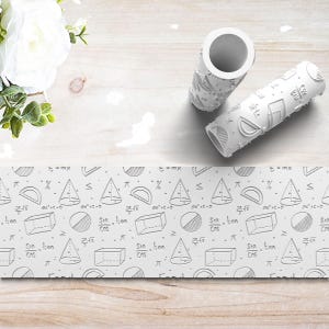 May include: Two white patterned rolling pins with geometric shapes and mathematical symbols. A white patterned paper strip with math symbols is also visible. The background is a light wood surface with white flowers.