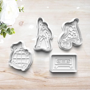 May include: Four white plastic cookie cutters in retro designs. The shapes include a disco ball, a figure in a jumpsuit, a roller skate with star details, and a cassette tape.