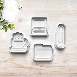 May include: Four white plastic cookie cutters shaped like a computer, a folder, a coffee cup, and a paperclip. The cutters are on a light brown wooden surface.