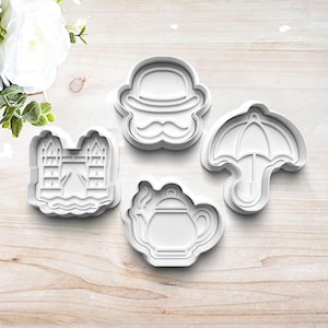 May include: Four white plastic cookie cutters in various shapes. The shapes include a London bridge, a bowler hat with a mustache, a teapot, and an umbrella. The cutters are arranged on a light wood-grain surface.