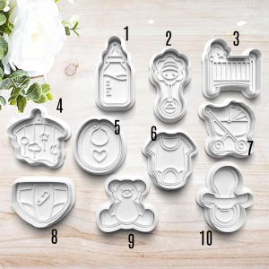 May include: Ten white plastic baby-themed cookie cutters. The cutters are numbered 1 through 10. The cutters include a baby bottle, rattle, crib, stroller, bib, onesie, teddy bear, pacifier, and diaper.