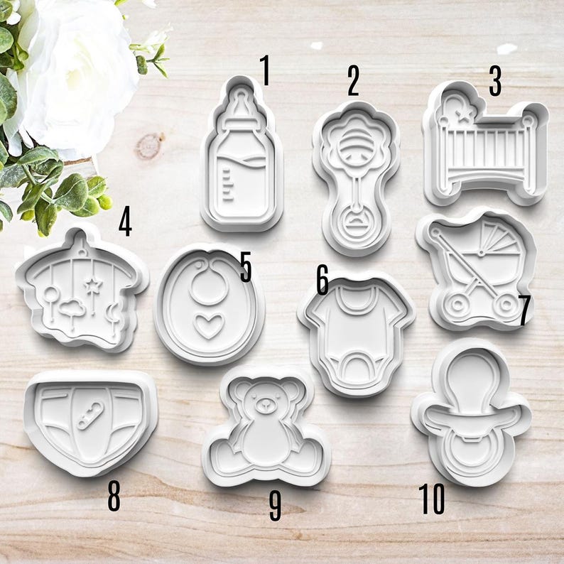 May include: Ten white plastic baby-themed cookie cutters. The cutters are numbered 1 through 10. The cutters include a baby bottle, rattle, crib, stroller, bib, onesie, teddy bear, pacifier, and diaper.