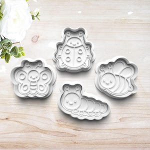 May include: A set of four white plastic cookie cutters featuring insect designs. The shapes include a ladybug, a butterfly, a bee, and a caterpillar. Each cutter has a raised outline and internal details to create impressions in dough.