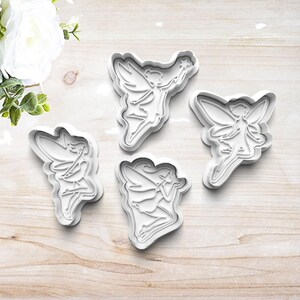 May include: Four white plastic cookie cutters shaped like fairies. Each fairy has wings, a dress, and a wand.