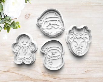 May include: Four white plastic cookie cutters shaped like Santa Claus, a snowman, a gingerbread person, and a reindeer.