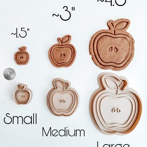 May include: Three cookie cutters in the shape of an apple, with a leaf on top. The cutters are labeled "Small", "Medium", and "Large". The cutters are approximately 1.5 inches, 3 inches, and 4.5 inches in diameter.