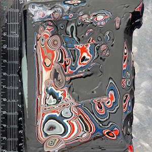 May include: A rectangular block of layered material featuring a marbled pattern of gray, red, white, and blue colors. A black ruler with white markings is positioned along the left and bottom edges, showing a width of 9 inches and height of 14 inches.